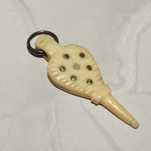 May include: A small, ivory-coloured bellows keychain with a silver-coloured ring. The bellows have small, round, brass-coloured accents. This decorative keychain could be vintage or antique.