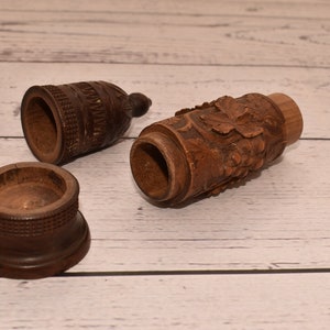 May include: Three wooden containers with intricate carvings. One container is cylindrical with a grapevine design, another is a small round container, and the third is a tall, cylindrical container with a geometric pattern.