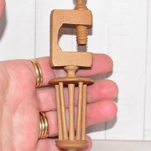 Könnte beinhalten: Eine hellbraune Nähklemme aus Holz mit einem C-förmigen Oberteil, das über einen Gewindeschraubmechanismus verfügt, und einer käfigartigen Unterkonstruktion aus vertikalen Stäben, die durch kreisförmige Scheiben verbunden sind.