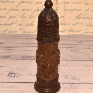 May include: A wooden bottle stopper with a carved grape design. The stopper has a rounded top and a base with a decorative band.