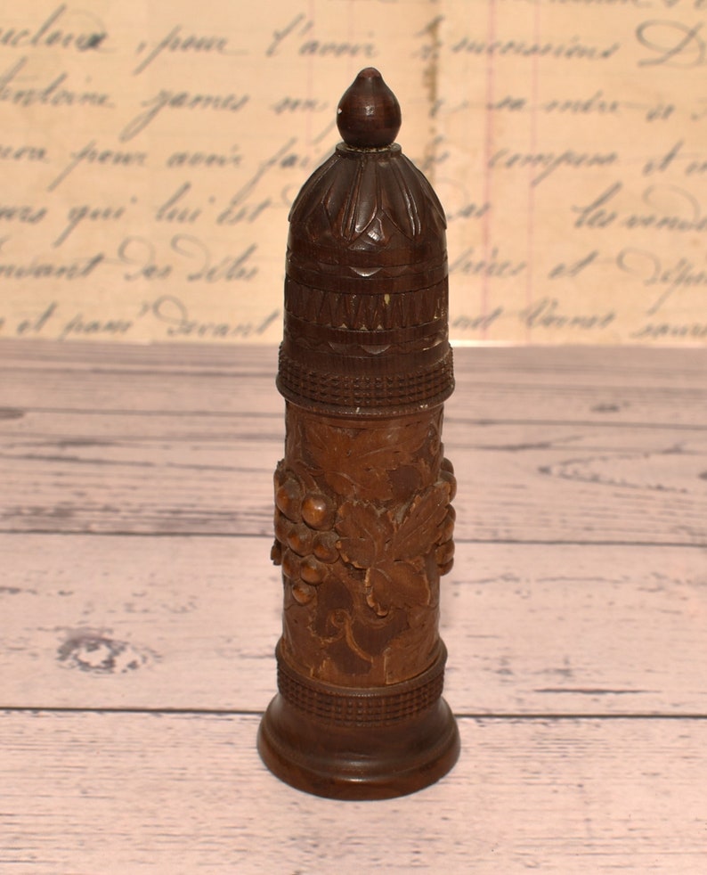 May include: A wooden bottle stopper with a carved grape design. The stopper has a rounded top and a base with a decorative band.