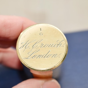 May include: A gold-colored metal cap with the inscription "1/6 H. Crouch. London."