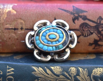 May include: A silver and gold brooch with a turquoise and gold inlay in the shape of a flower.