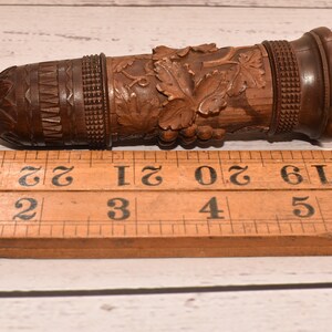 May include: A wooden carved bottle stopper with a grapevine design. The stopper is 3 inches long and has a dark brown finish.