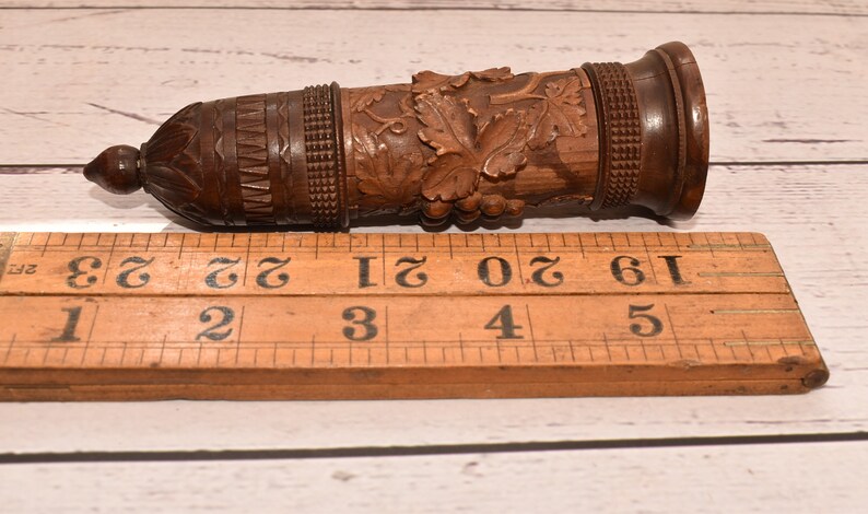 May include: A wooden carved bottle stopper with a grapevine design. The stopper is 3 inches long and has a dark brown finish.
