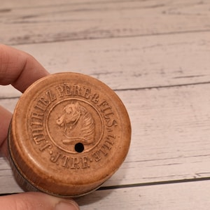 Op de afbeelding: Een ronde, bruine blikken doos met een paardenkoplogo en de tekst "J.T.P.F.  THIRL  PERE & FILS" op het deksel.