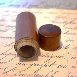 Puede incluir: Un recipiente de madera con tapa, ambos hechos de madera marrón oscuro. El recipiente está abierto y el interior es visible. El recipiente está sobre un trozo de papel con texto escrito a mano.