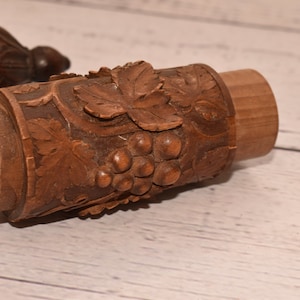 May include: A wooden carved container with a grapevine design. The container is made of dark brown wood and has a detailed carving of grapes and leaves.