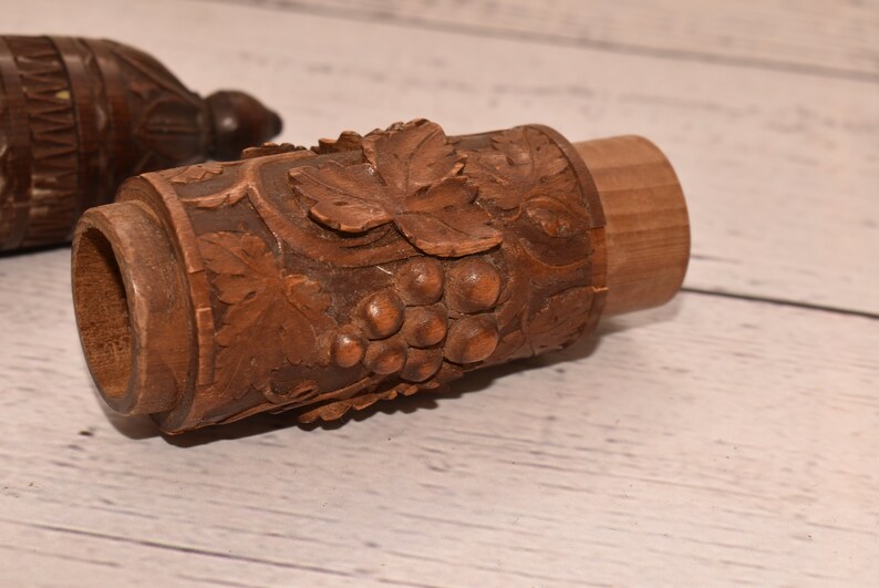May include: A wooden carved container with a grapevine design. The container is made of dark brown wood and has a detailed carving of grapes and leaves.