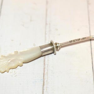 May include: An antique silver and mother-of-pearl button hook. The handle is carved in a leaf design, and the silver shaft has a hook on one end. The hook is approximately 15 cm long.