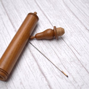 May include: A wooden needle case with a small wooden stopper and a long, thin needle. The case is brown and has a smooth finish.