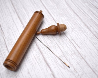 May include: A wooden needle case with a small wooden stopper and a long, thin needle. The case is brown and has a smooth finish.