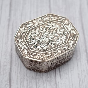 Peut inclure: Une boîte à bijoux octogonale en argent avec un motif floral complexe.