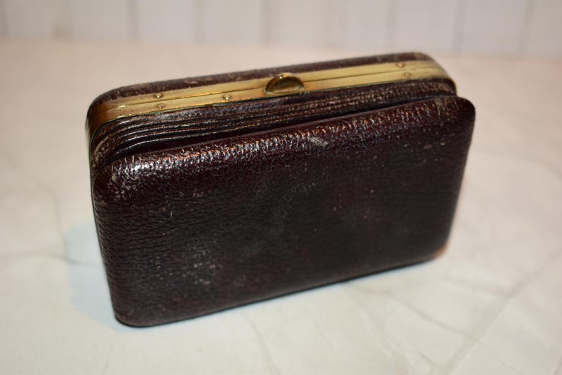 May include: A vintage, rectangular, dark brown leather wallet with a textured surface. The wallet has a gold-coloured metal frame and clasp. The wallet is slightly open, revealing the interior.