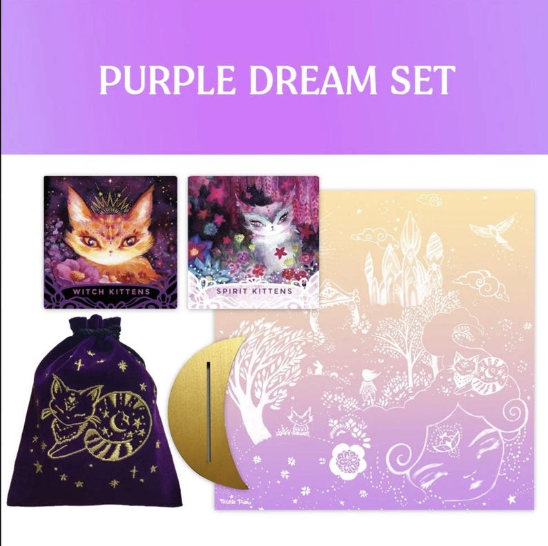 Może przedstawiać: Zestaw Purple Dream z ilustrowanymi kartami z wizerunkami kot&oacute;w, aksamitnym workiem ze złotym haftem i złotym p&oacute;łksiężycem. Zestaw zawiera tekst "Witch Kittens" i "Spirit Kittens". Tło to gradient fioletu i ż&oacute;łci.