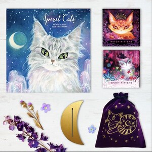 Może przedstawiać: Kolekcja przedmiot&oacute;w z motywem kota, w tym kalendarz "Spirit Cats" 2026, dwa wydruki "Witch Kittens" i "Spirit Kittens", złoty stojak w kształcie p&oacute;łksiężyca, fioletowy aksamitny woreczek i akcenty kwiatowe.