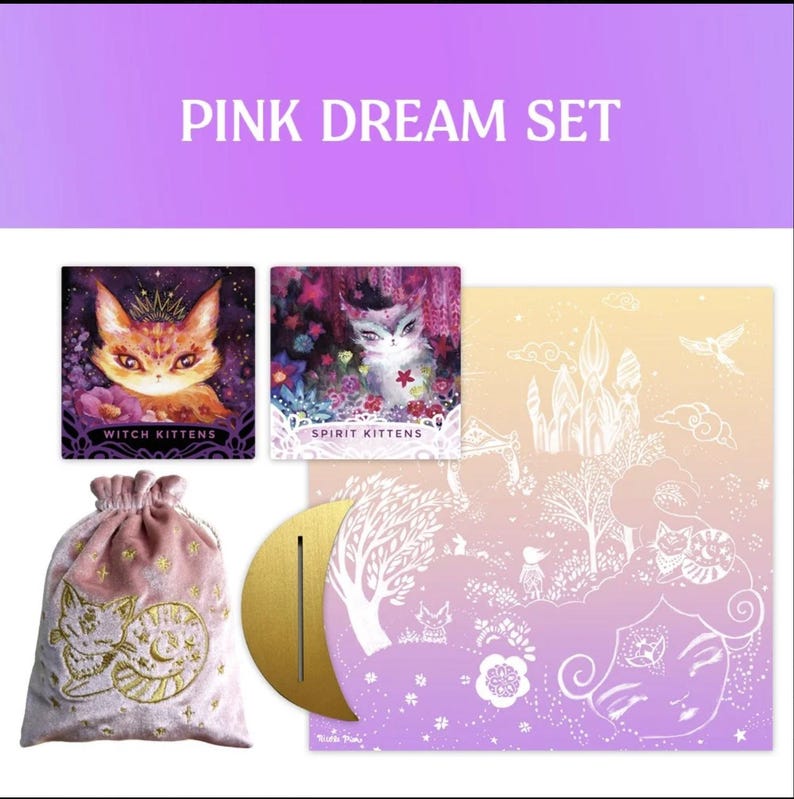 Może przedstawiać: Zestaw Pink Dream z ilustrowanymi kartami z kotami, woreczkiem ze sznurkiem ze złotym haftem i złotym stojakiem w kształcie p&oacute;łksiężyca. Karty przedstawiają projekty takie jak "Witch Kittens" i "Spirit Kittens". Zestaw ma motyw fantasy.