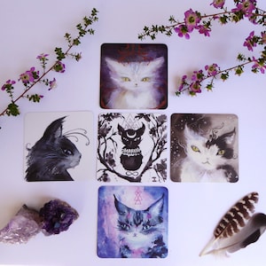 Pode incluir: Cinco cartas de tar&ocirc; com ilustra&ccedil;&otilde;es em preto e branco de gatos. As cartas est&atilde;o dispostas em forma de cruz sobre um fundo branco. As cartas s&atilde;o cercadas por flores roxas e uma pena.