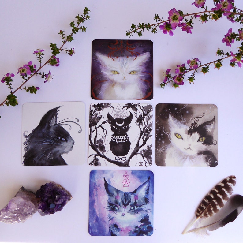 Pode incluir: Cinco cartas de tar&ocirc; com ilustra&ccedil;&otilde;es em preto e branco de gatos. As cartas est&atilde;o dispostas em forma de cruz sobre um fundo branco. As cartas s&atilde;o cercadas por flores roxas e uma pena.