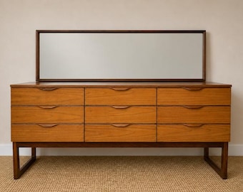 May include: A rectangular wooden chest of drawers featuring nine drawers arranged in three vertical columns. Each drawer has a carved horizontal handle. A large, rectangular mirror with a dark brown wooden frame is positioned directly above the unit.