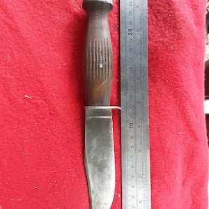 May include: A vintage hunting knife with a wooden handle and a stainless steel blade. The blade measures approximately 4 inches. The knife is placed on a red surface next to a ruler.