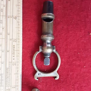 May include: A brass whistle with a black plastic top and a ring handle. The whistle is marked "16" and "A.E. LISTER 3".
