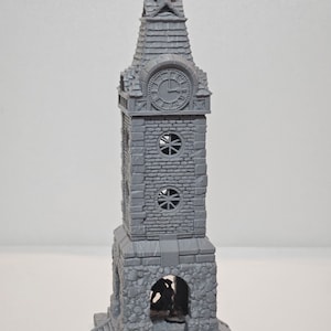 May include: A gray miniature clock tower with a detailed stone facade, a clock face, and a pointed roof. The tower has arched openings and circular windows. A small figurine stands at the base, suggesting a fantasy or tabletop game theme.