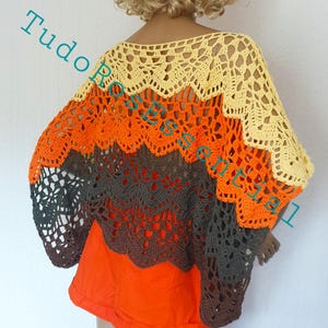 Könnte beinhalten: Ein handgefertigter Häkelponcho in Gelb-, Orange-, Braun- und Grautönen. Das offene Design hat einen gewellten Rand und wird über einem orangefarbenen Oberteil getragen. Der Text "Tudo Roses" ist auf dem Kleidungsstück zu sehen.