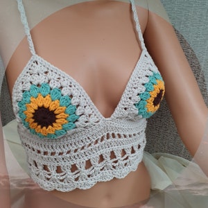 May include: A white crocheted crop top with a sunflower design. The top has a V-neck and adjustable straps.