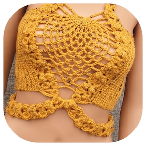 May include: Mustard yellow crochet top with a halter neck and a lattice design. The top features a floral pattern around the edges and a connecting strap that wraps around the waist. The crochet work has small flecks of darker color.