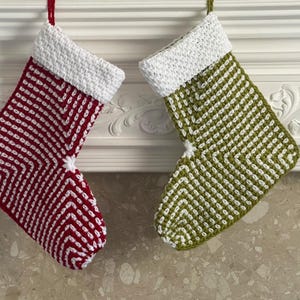 May include: Two handmade Christmas stockings. One is red with white zig-zag stripes, the other is green with white zig-zag stripes. Both have white cuffs and red or green hanging loops. The stockings are hanging on a white mantel.