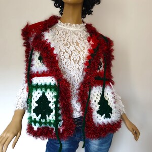 May include: A handmade Christmas vest featuring a festive design. The vest is primarily red with white and green accents, and a shaggy trim. The front panels display a Christmas tree motif. The vest is worn over a white lace top and blue jeans.