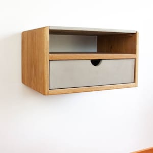 May include: A wall-mounted nightstand with a drawer and a shelf. The nightstand is made of wood with a light brown finish and has a gray concrete top.