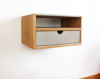 May include: A wall-mounted nightstand with a drawer and a shelf. The nightstand is made of wood with a light brown finish and has a gray concrete top.
