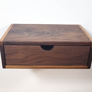 May include: A dark brown wooden floating shelf with a single drawer. The shelf has a light brown wood trim around the edges.