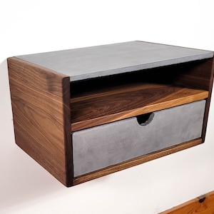 May include: A floating walnut wood nightstand with a concrete top and drawer. The drawer has a concrete front and a walnut wood frame.