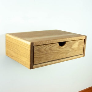 May include: A light wood floating bedside table with a single drawer. The drawer has a slightly rounded cutout for the handle.