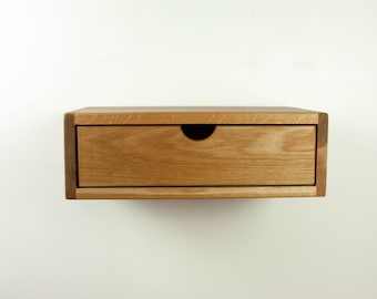 May include: A wooden wall-mounted shelf with a single drawer. The drawer is made of light wood and has a black pull.