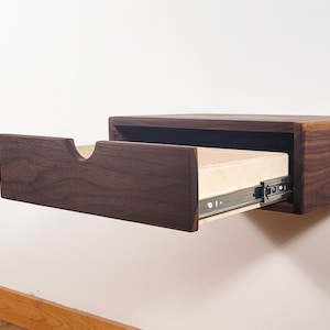 May include: A dark walnut wood floating shelf with a drawer that is partially open. The drawer is made of light wood and has a metal slide.