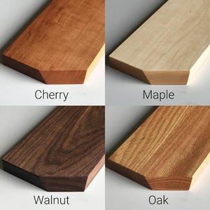 May include: Close-up of four wood samples: cherry, maple, walnut, and oak. Each sample is a rectangular piece of wood with a beveled edge.
