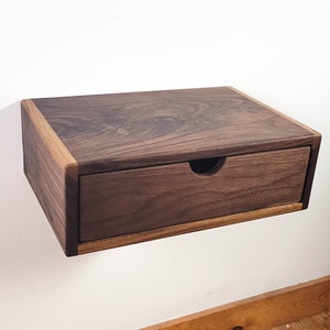 May include: A wall-mounted wooden shelf with a drawer. The shelf and drawer are made of dark walnut wood with a light wood trim.
