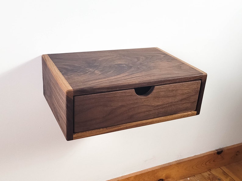 May include: A wall-mounted wooden shelf with a drawer. The shelf and drawer are made of dark walnut wood with a light wood trim.