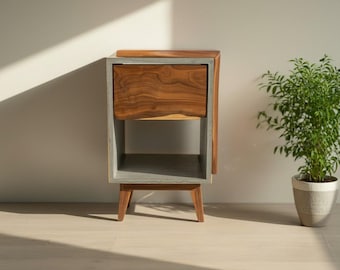 May include: A bedside table featuring a rectangular gray concrete frame with a single wooden drawer showcasing a natural wood grain pattern. The unit is supported by four angled wooden legs and includes an open storage shelf below the drawer.
