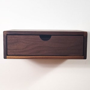 May include: A dark brown wooden floating shelf with a single drawer. The drawer is made of the same wood and has a simple, modern design.