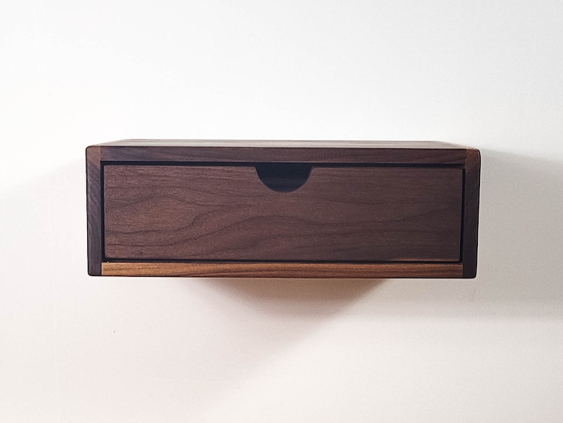 May include: A dark brown wooden floating shelf with a single drawer. The drawer is made of the same wood and has a simple, modern design.
