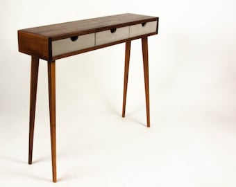 May include: A wooden console table with three drawers and tapered legs. The table top is made of dark wood and the drawers are white.