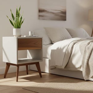 May include: A bedside table featuring a white frame, a single wooden drawer, and an open storage shelf underneath. The table is supported by four tapered wooden legs and holds a white potted snake plant and a small white cup on its top surface.