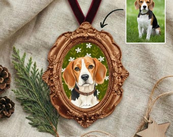 May include: A framed beagle portrait ornament with a brown and gold ornate frame, a green background with white flowers, and a red velvet ribbon. The ornament includes a small portrait of the beagle. The ornament is displayed on a neutral linen surface.