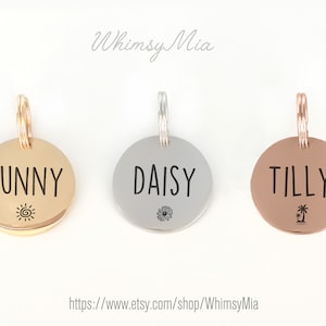 May include: Three round pet tags in gold, silver, and rose gold. Each tag has a name in black text: "SUNNY", "DAISY", and "TILLY". Sunny has a sun graphic, Daisy a flower, and Tilly a palm tree.