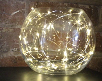 May include: A clear glass globe filled with white fairy lights. The lights are strung throughout the globe, creating a warm and inviting glow.